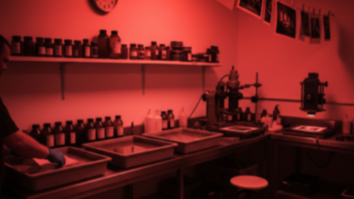 フィルム写真時代の伝統的な暗室作業風景。赤い光の中で行われる、手作業による写真現像のプロセス。