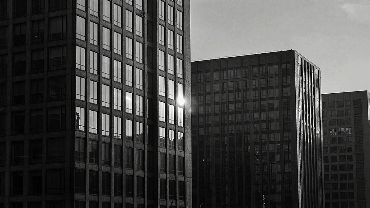 「光画」というテーマを象徴する、ビルの窓に鋭く反射する太陽の光。無機質なビルのグリッドと対照的な強い輝きが、写真の本質である「光」を強調している。